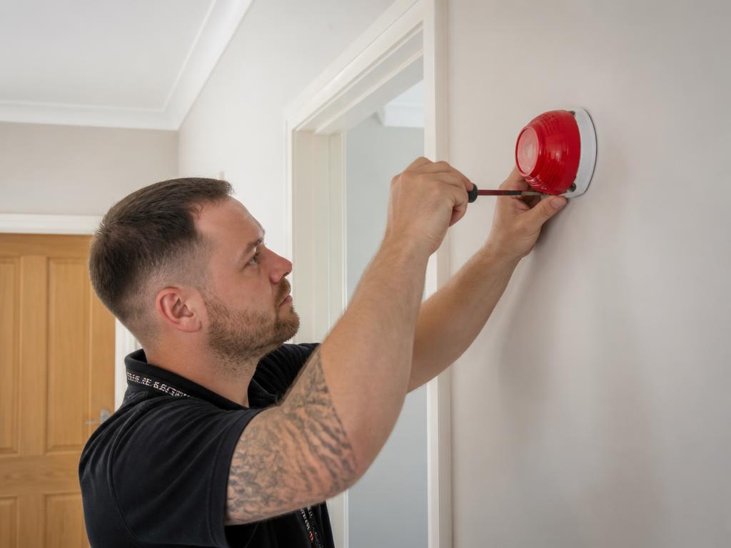 Technician installing a residential fire alarm sounder on a hallway wall in a calm, everyday setting